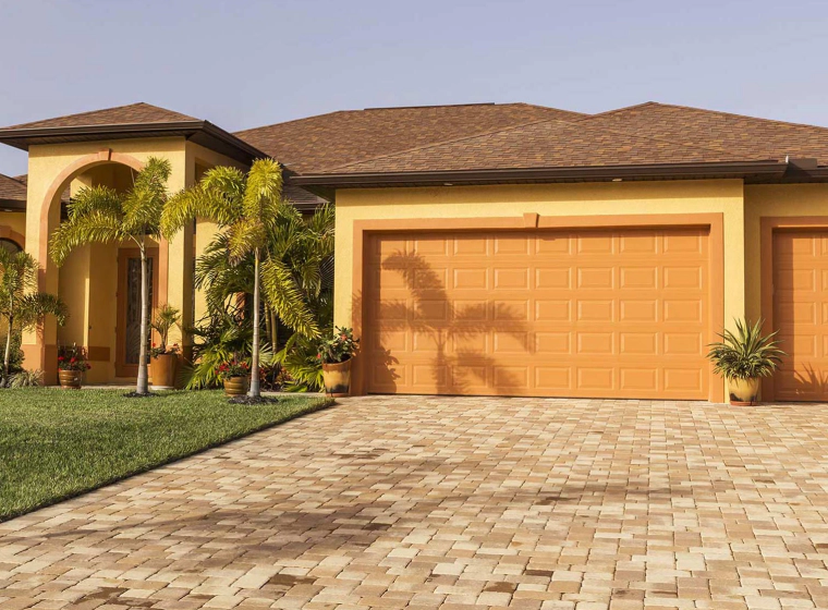 yellow house with orange doors and sidings with palms outside and a driveway